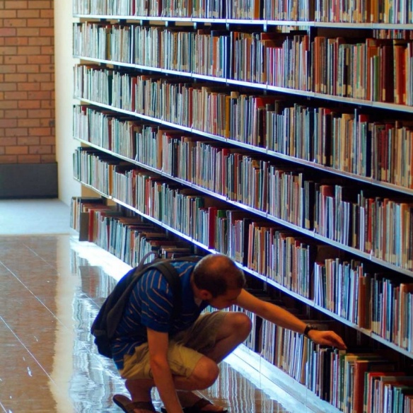 Student searching for a book in book stacks in a library.