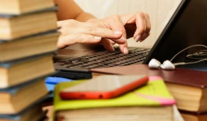 A student working on a laptop among a pile of books. 