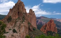 Brandy Petrie's photo of Garden of the Gods Park in Colorado Springs. Depicted: a colorful landscape with green foliage and trees, blue skies with clouds, and reddish rock formations. 