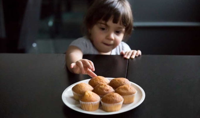 Child reaching for a plate of muffins. 