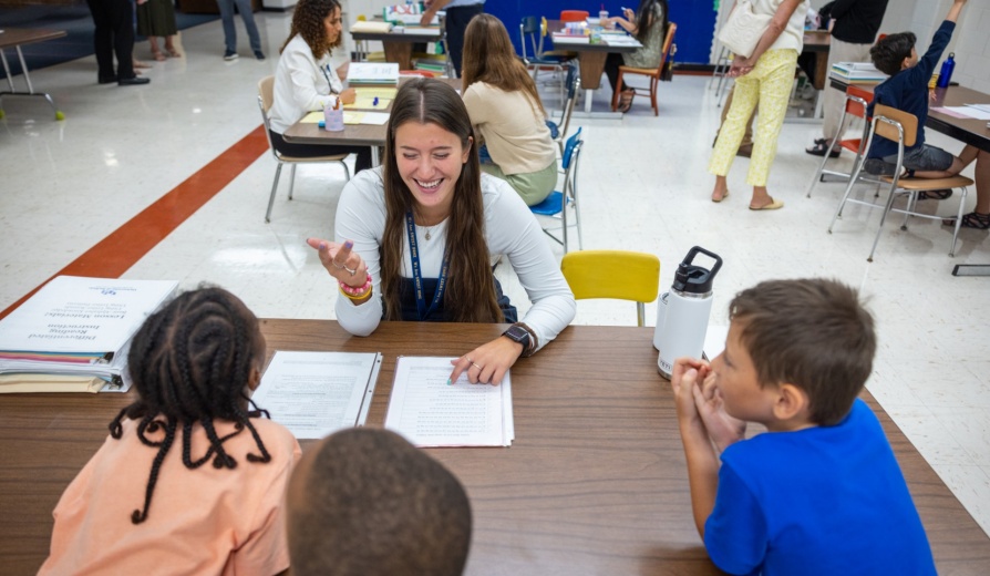 Young students at a desk with a teacher. 