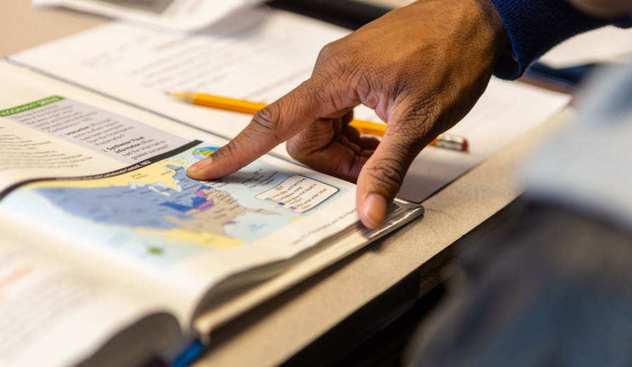 Teacher's hand pointing to a map of the Unites States in a social studies textbook. 