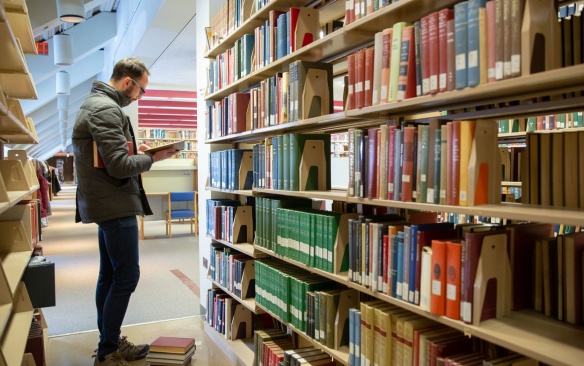 Student reading a book in Lockwood Library book stacks. 