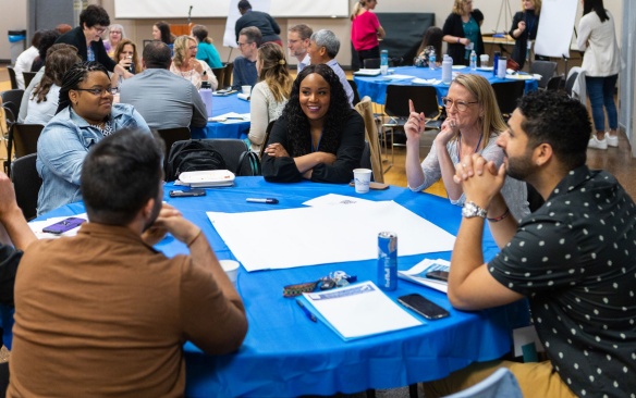 Students gathered at a conference in conversation with faculty. 