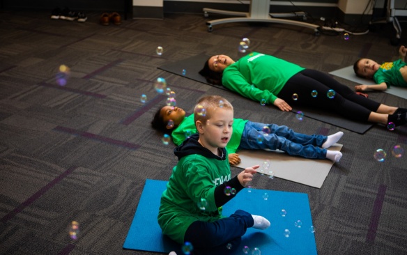 Catherine Cook-Cottone, professor of counseling, school and educational psychology, and Claire Cameron, associate professor of learning and instruction, study how yoga and mindfulness-based programs for children help establish body awareness, decrease anxiety and assist stress management. Vito Gigante, director of occupational therapy at the Beyond Learning Center (formerly the Cantalician Center for Learning) leads young children in a yoga practice. Photographer: Douglas Levere. 