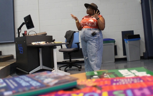 Dawnavyn James in front of books, giving a speech to a classroom. 