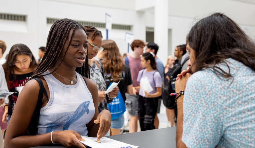 Student at a registration table in conversation with an advisor. 