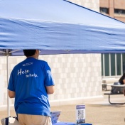 Male student standing at an outdoor information tent. 