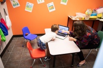 Faculty researcher working with a child on a laptop in a classroom. 