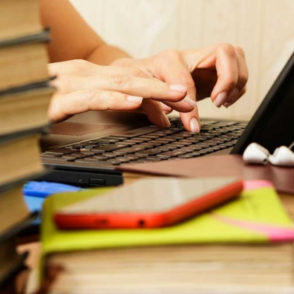 A student working on a laptop among a pile of books. 