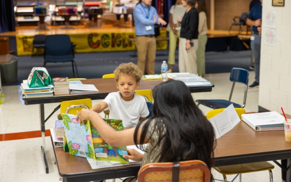 A young student looks at a book his tutor is holding up. 