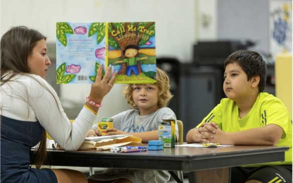 Young students listening to their teacher read a book. 