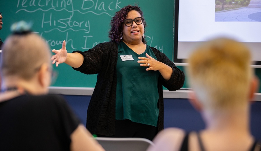 A person stands at the front of a classroom and gestures while conducting a conference session. 