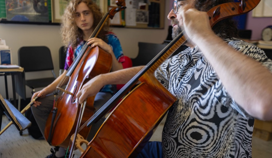 Student working with a music professor in a one-on-one cello lesson in an office space in Baird Hall. 