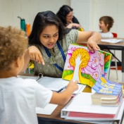 Teacher reads a book to her student. 