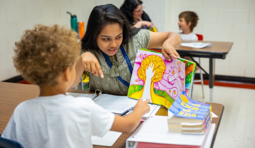 Teacher reads a book to her student. 