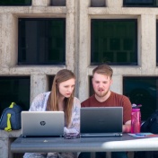 Two students working together on laptops outside on UB's North Campus. 