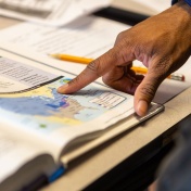 Teacher's hand pointing to a map of the Unites States in a social studies textbook. 