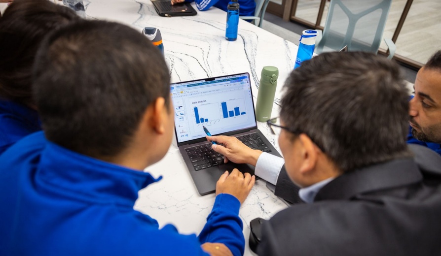 Students and a professor gathered around a laptop analyzing data report. 