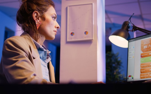 Woman working late on a computer analyzing data reports. 