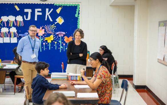 Two teachers stand and observe a tutor and student. 