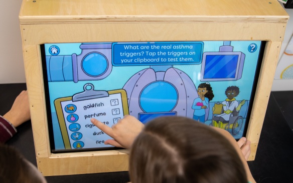 Student touches computer screen with word matching game. 