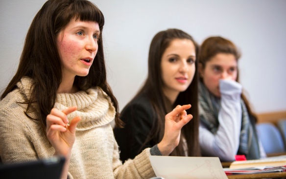 College students sitting at desks speaking. 