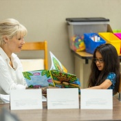 A tutor at the front of a classroom with her student as they read. 