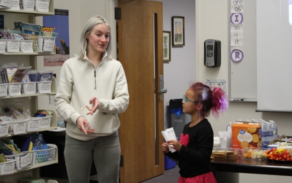 A tutor at the front of a classroom with her student as they read. 