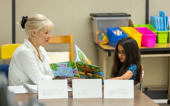 A tutor at the front of a classroom with her student as they read. 