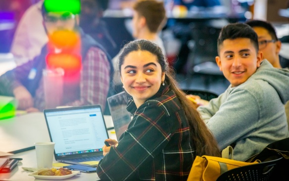 Students gathered together with laptops smiling. 