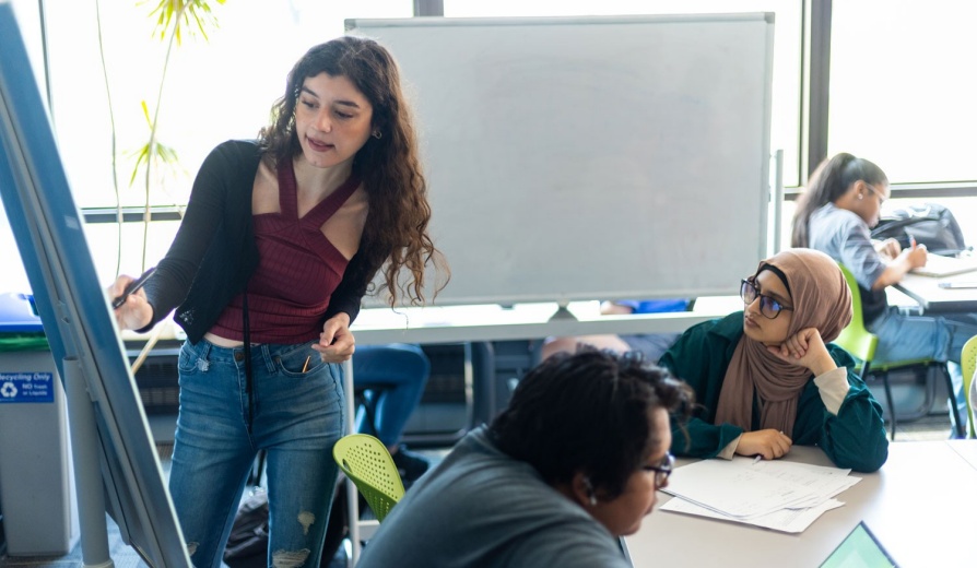 An undergraduate student presenting data on a white board. 