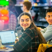 Students gathered together with laptops smiling. 