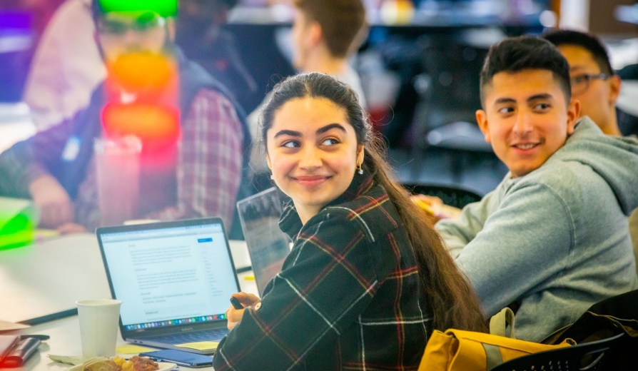 Students gathered together with laptops smiling. 