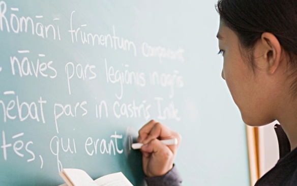 Student wriging in Latin on a blackboard. 