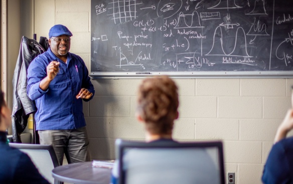 Teacher with students in a classroom teaching physics lesson on blackboard. 