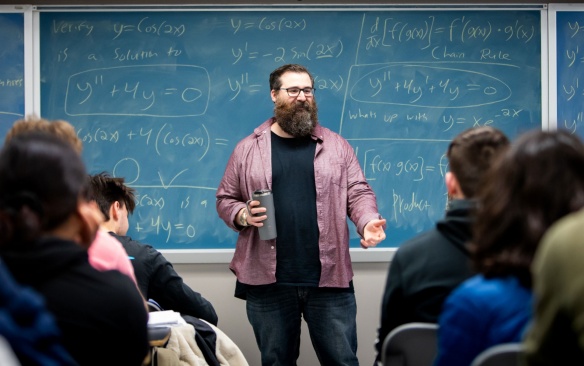 Teacher with students in a classroom teaching math lesson on blackboard. 