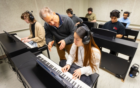 Teacher with students in a classroom teaching piano lesson. 