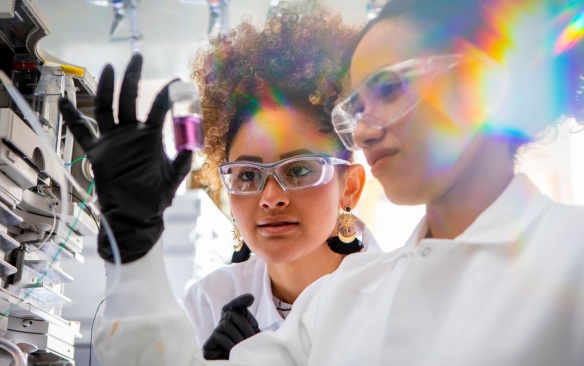 Two female students in a lab with a bottle of chemicals. 