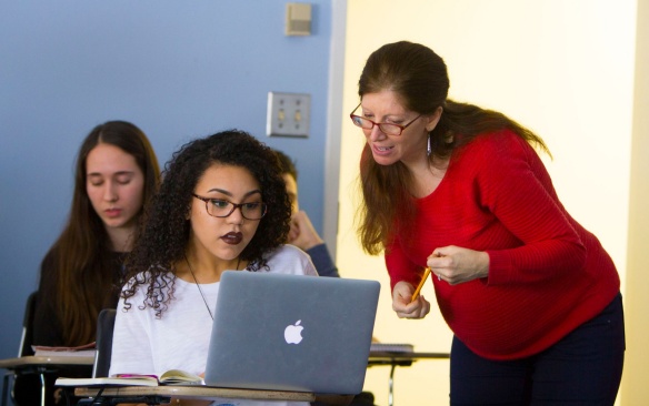 Teachers helping a student in class on a laptop. 