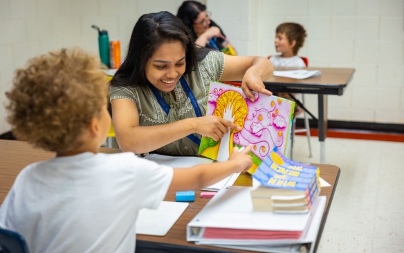 Student teacher reading a book with a student in a classroom. 