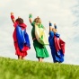 Children in super hero costumes with arms raised energetically. 