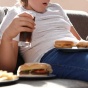 Child eating burgers and drinking soda on a couch while watching a phone. 