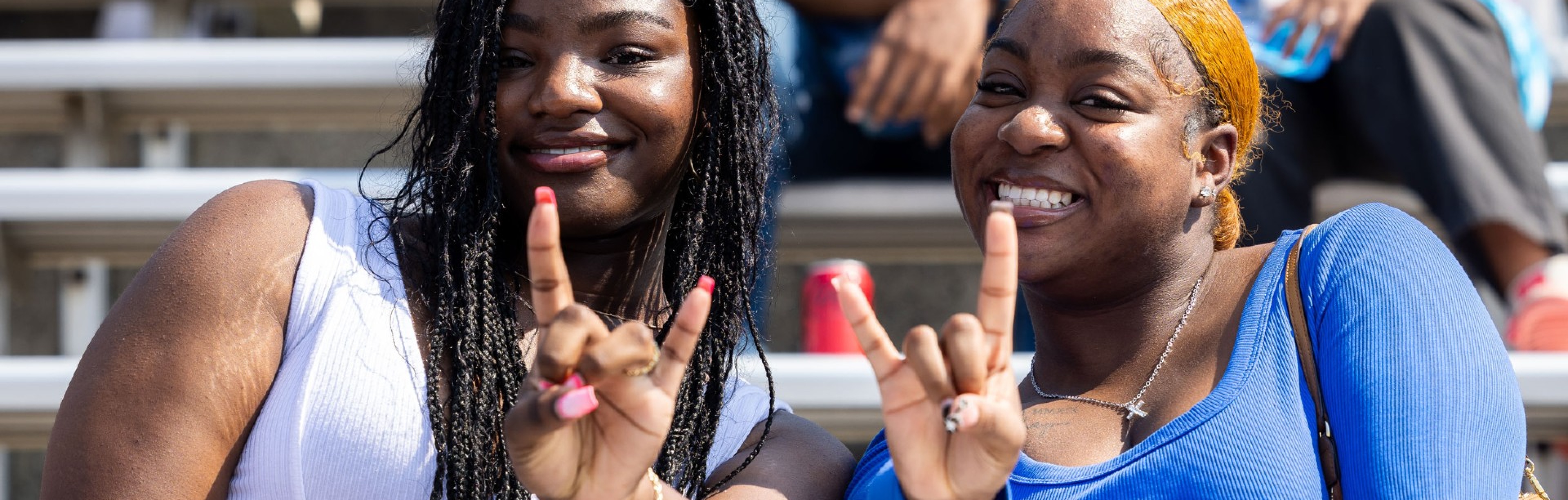 Students celebrating at a football game giving the horns up symbol. 