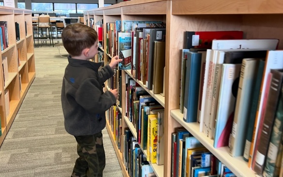 Child looking through book stacks in a library. 