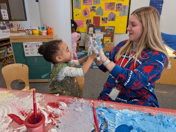 A student and teacher play in the classroom with messy colorful shaving cream. 