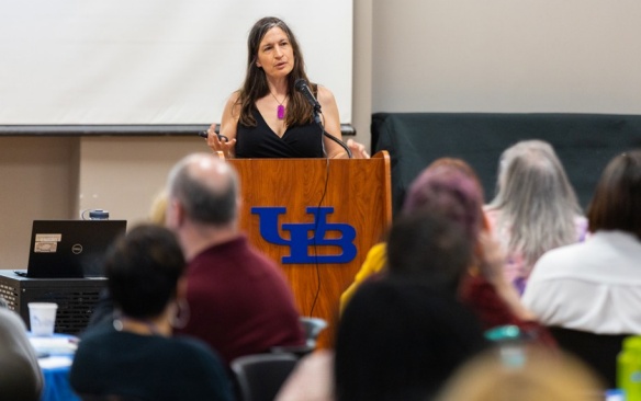 Margaret Sallee at a UB branded podium speaking in front of a crowd. 