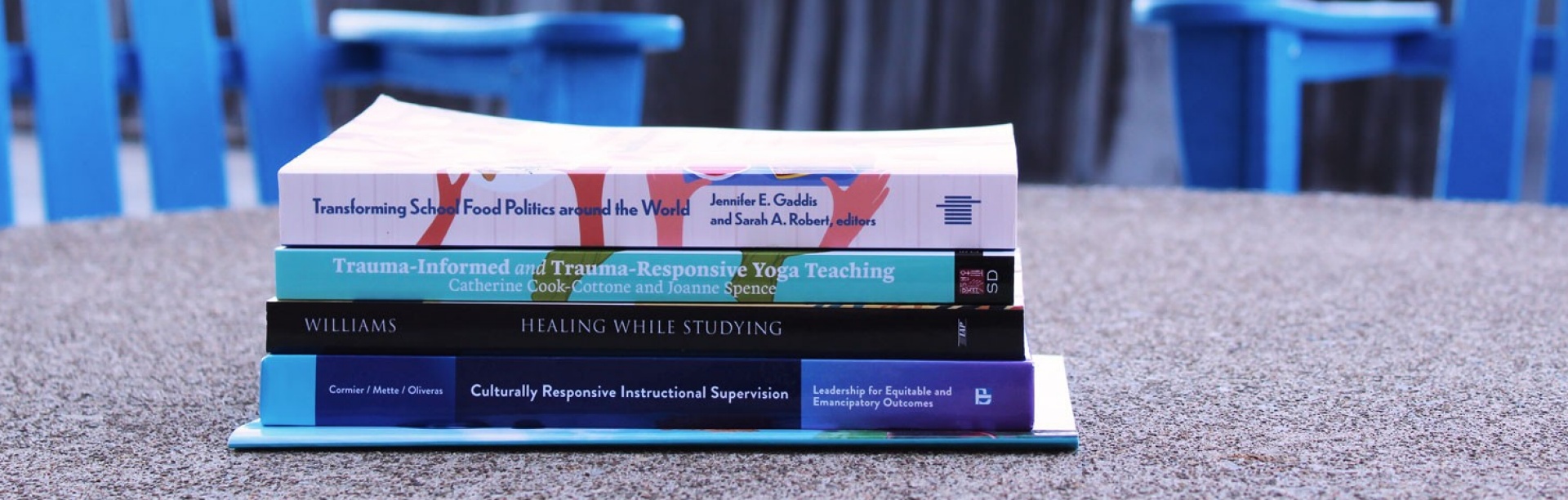 Books by GSE faculty and alumni stacked on top of one another on an outdoor table. 