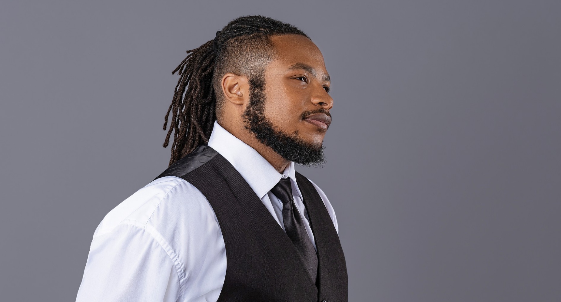 Dorian Winthrow in a suit, vest and white collared shirt, in front of a grey background. 