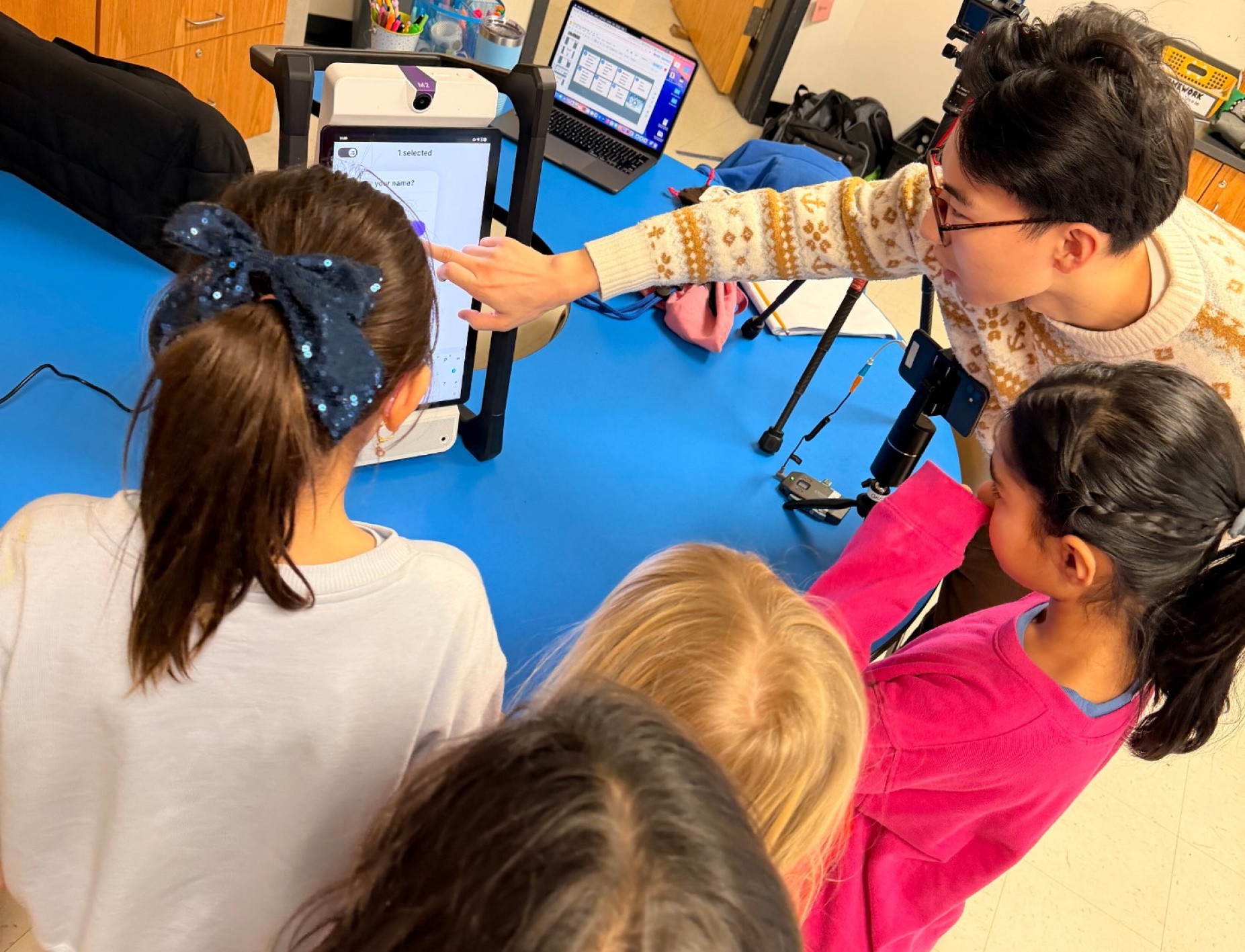 Four elementary students gather around the M2 device with their teacher. 